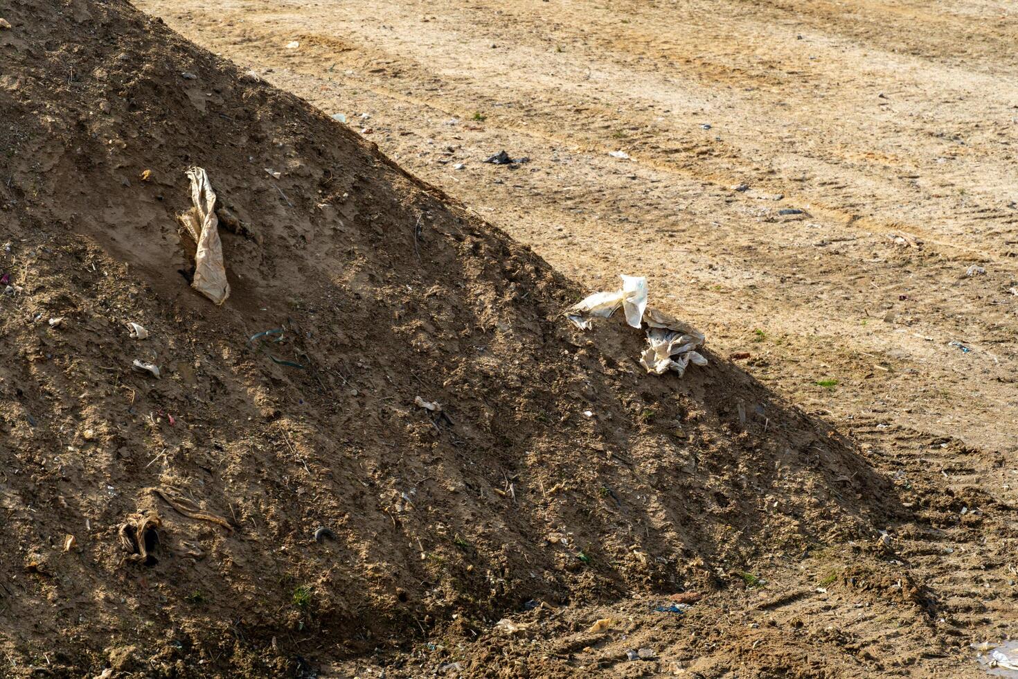 Earth mound containing discarded refuse debris exhibiting environmental contamination and terrain disturbance with tire tracks. photo