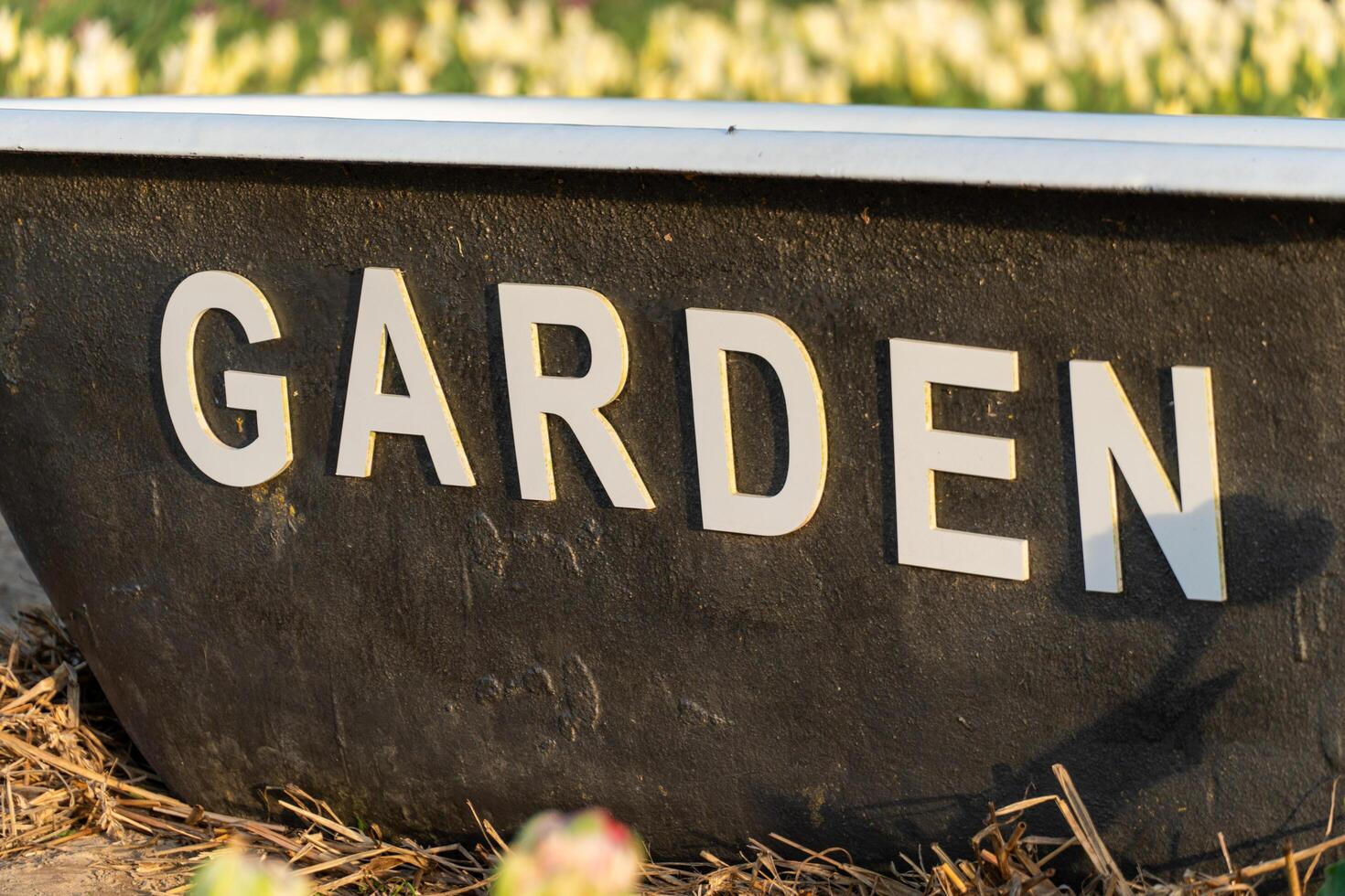 Black Garden Planter Container Box with White Lettering near Flowers in a Green Yard Background Scene for Gardening Concepts photo
