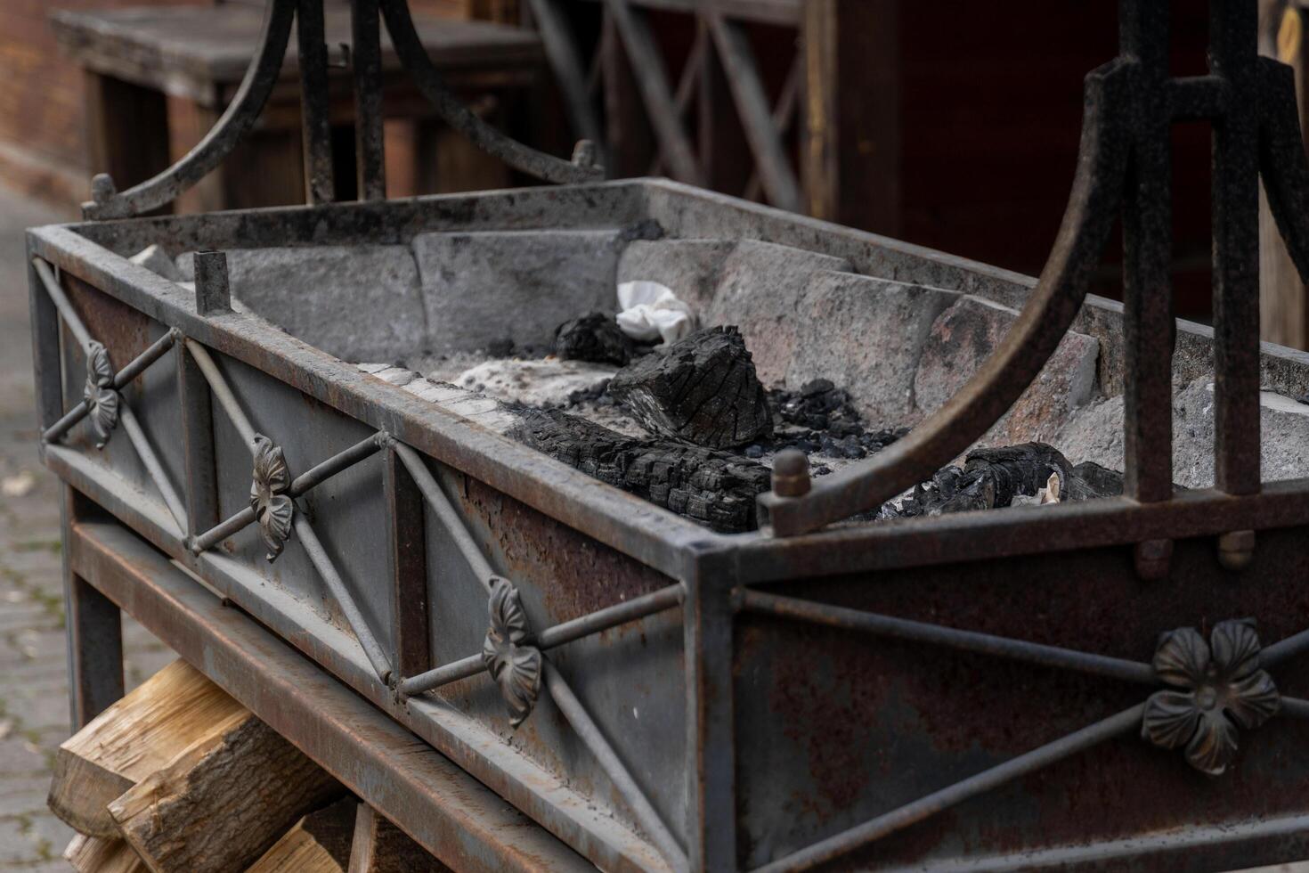 Rustic metal fire pit with burned logs and wood storage underneath displaying signs of age and weathered use. photo