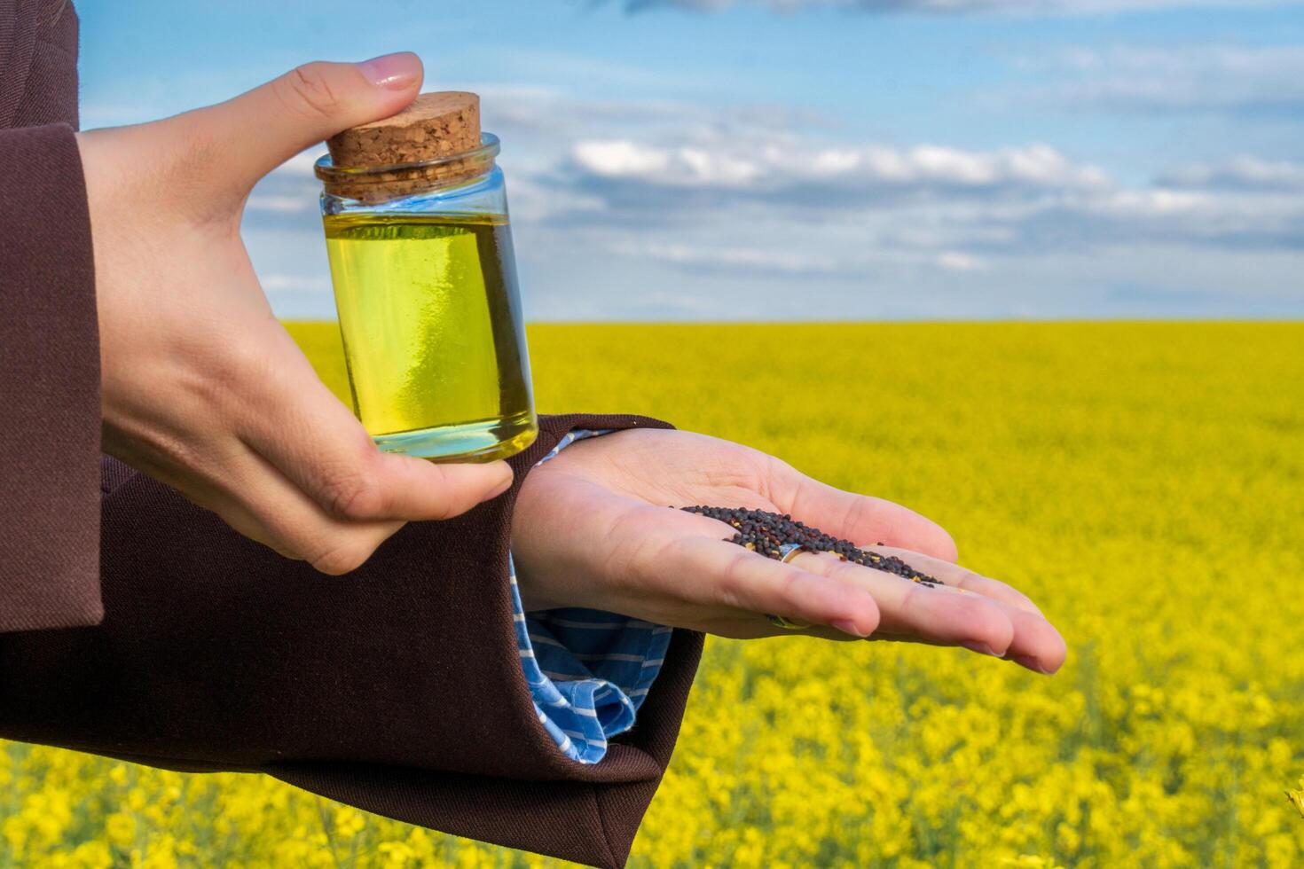 Hands hold a jar of biofuel while seeds are poured from the palm, set against a vast yellow field under a bright sky, highlighting renewable energy potential photo