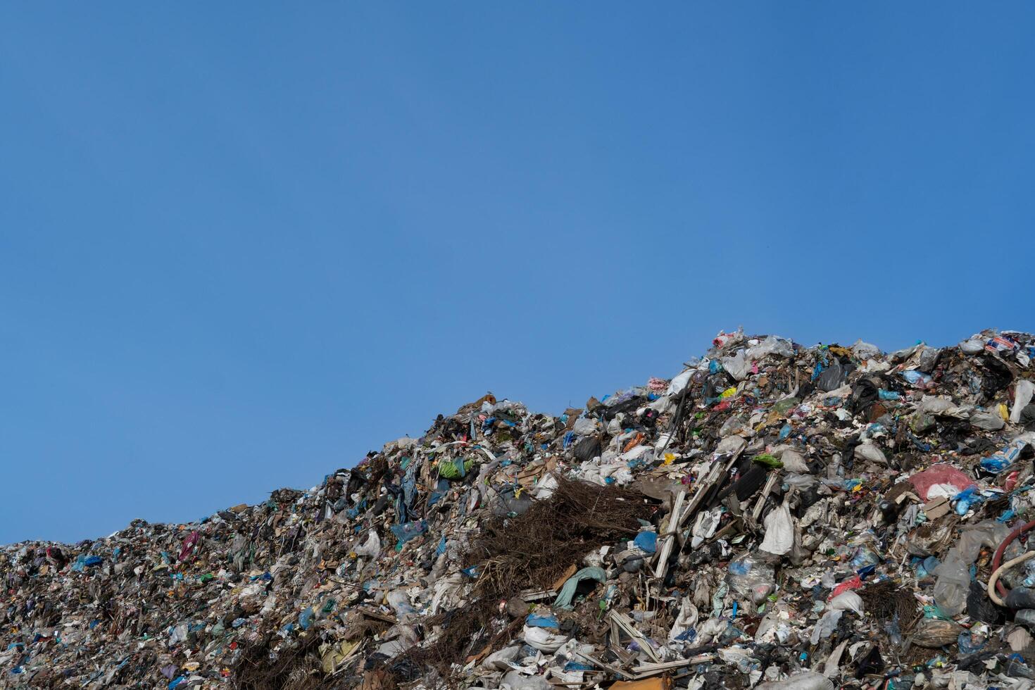 Overfilled landfill with diverse waste materials against clear blue sky illustrating environmental problems and unsustainable consumption habits photo