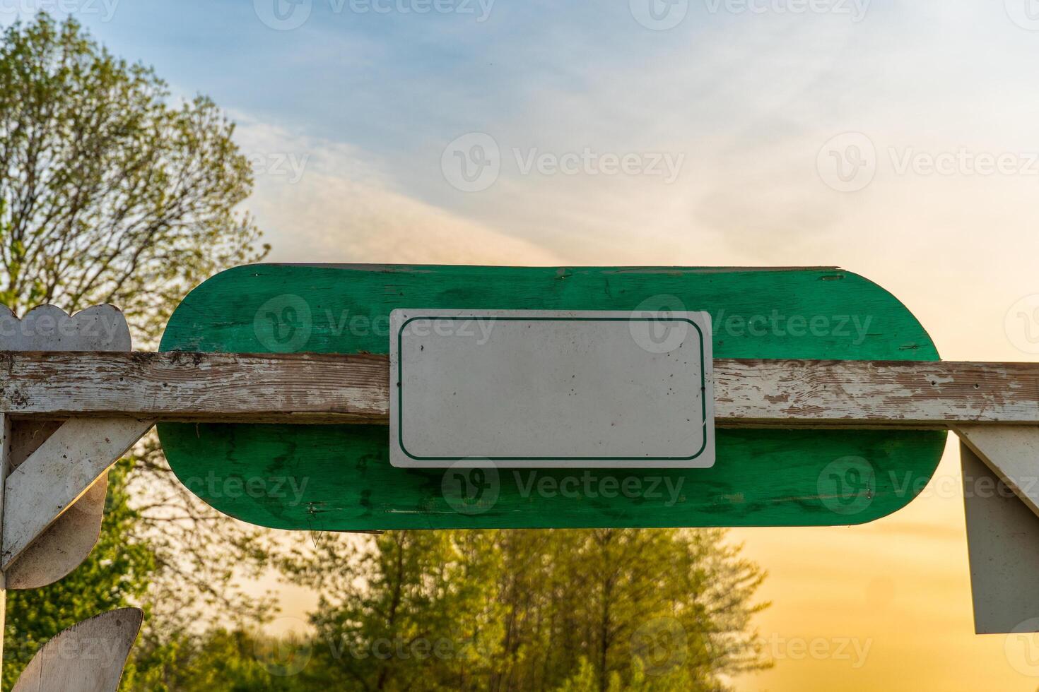 Vintage blank white road sign with green wooden frame during dusk against blurred trees and peaceful sky photo