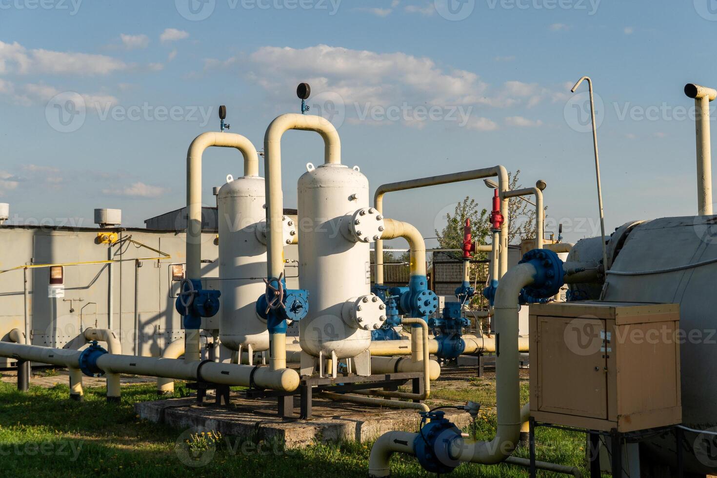 Industrial landscape with white tanks, blue valves and metal pipes against cloudy sky in outdoor industrial environment photo
