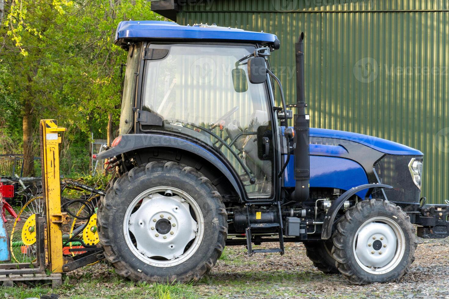 Blue Farm Tractor Parked on Gravel Surface with Attached Agricultural Equipment photo