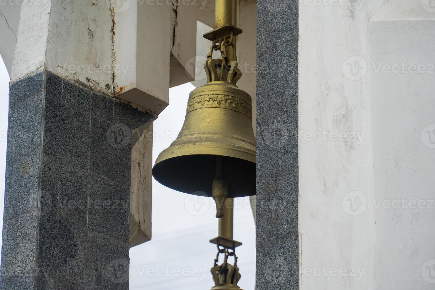 A large brass bell is suspended in a tower, featuring detailed craftsmanship photo