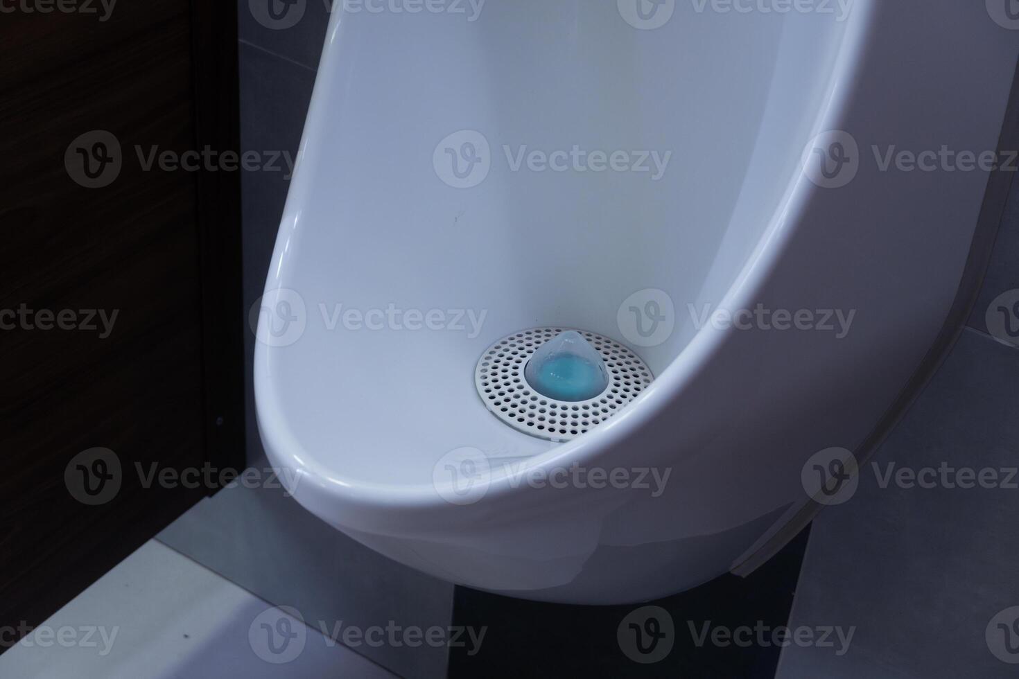 A well-maintained restroom fixture showcases a modern design, featuring a urinal with a blue deodorizing disk placed in its drain area photo