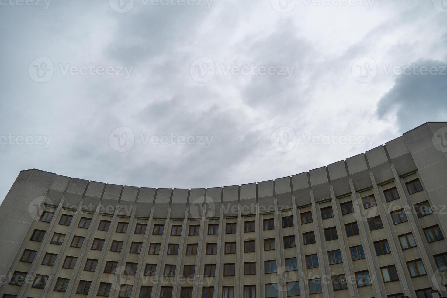 A contemporary structure with numerous windows stands against an overcast sky. The building's curved design highlights modern architectural trends, creating a striking silhouette photo