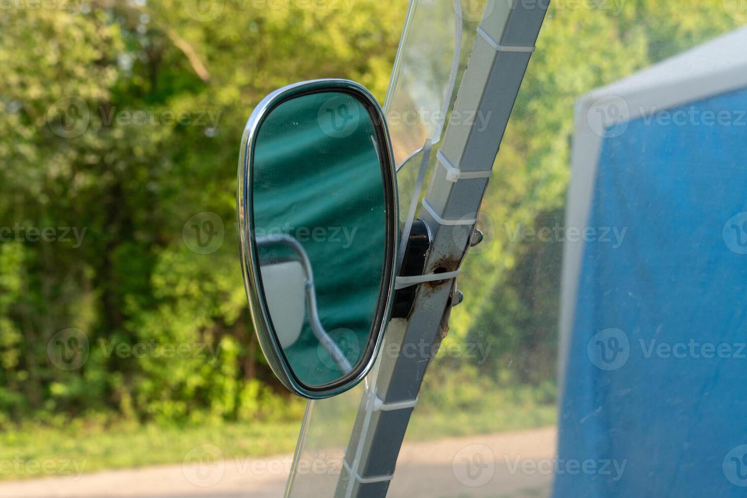 A side mirror reflects a vibrant green backdrop of trees along a tranquil country road in the early morning. The clear weather enhances the serene atmosphere photo