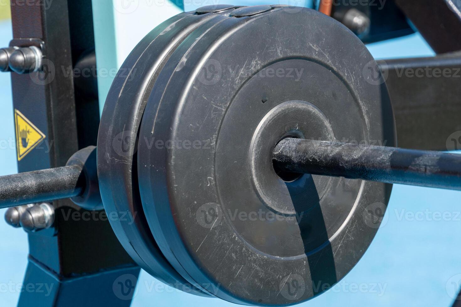 Close-up view of heavy weight plates secured on a barbell in an outdoor gym setup, ready for a rigorous workout session under clear blue skies photo