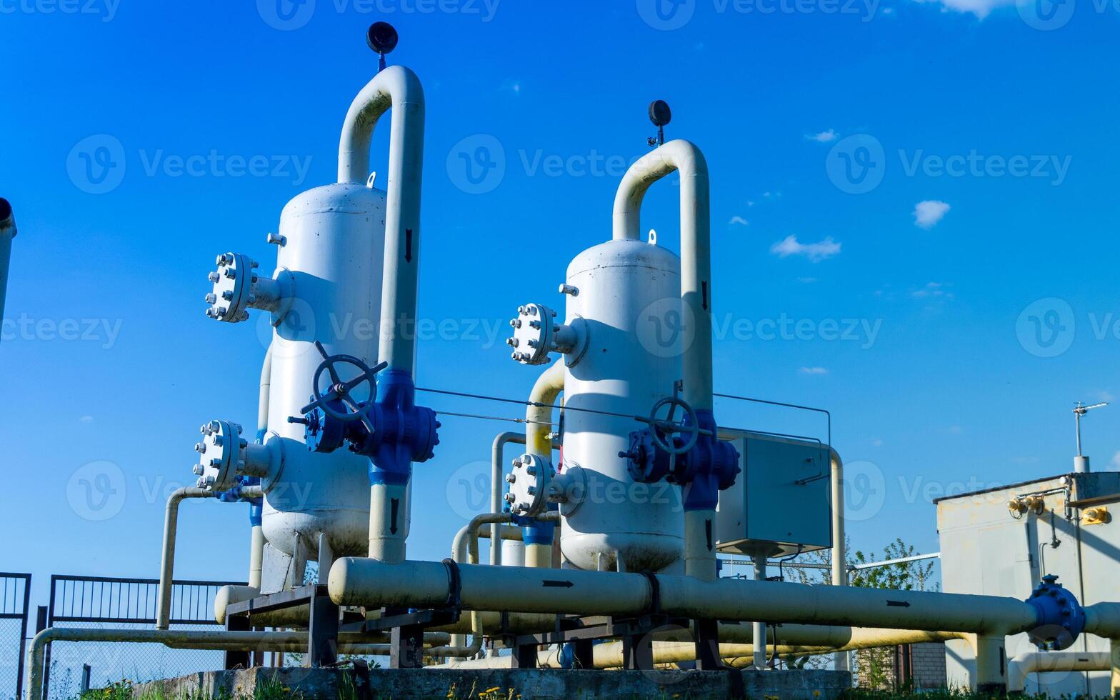 Two large gas processing units with valves and piping stand prominently against a bright blue sky at a manufacturing site during the day photo