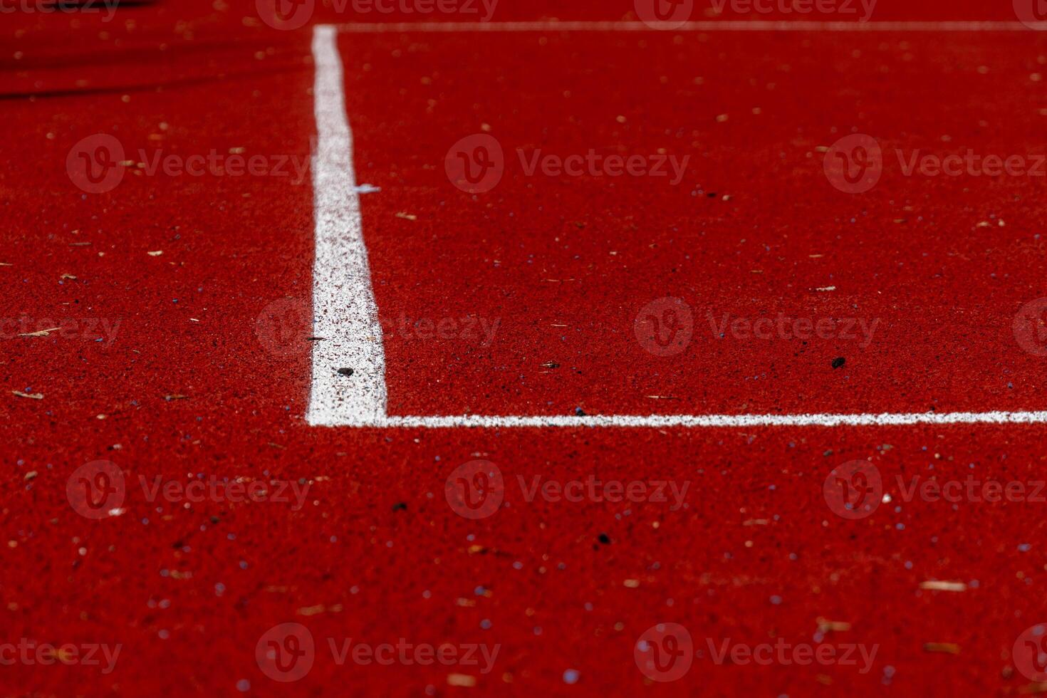 A vibrant red running track features a precise white line marking a lane boundary. Various debris is visible on the surface, indicating recent activity photo