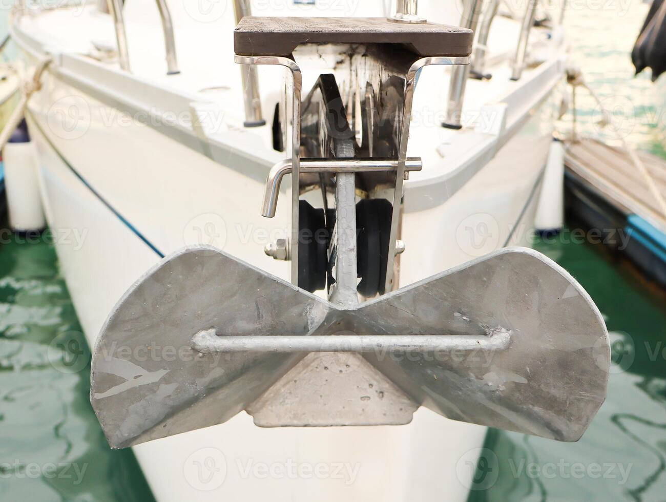 Close-up view of a modern yacht anchor mounted at the bow, docked in clear greenish water. Nautical equipment detail with visible textures and reflections. photo