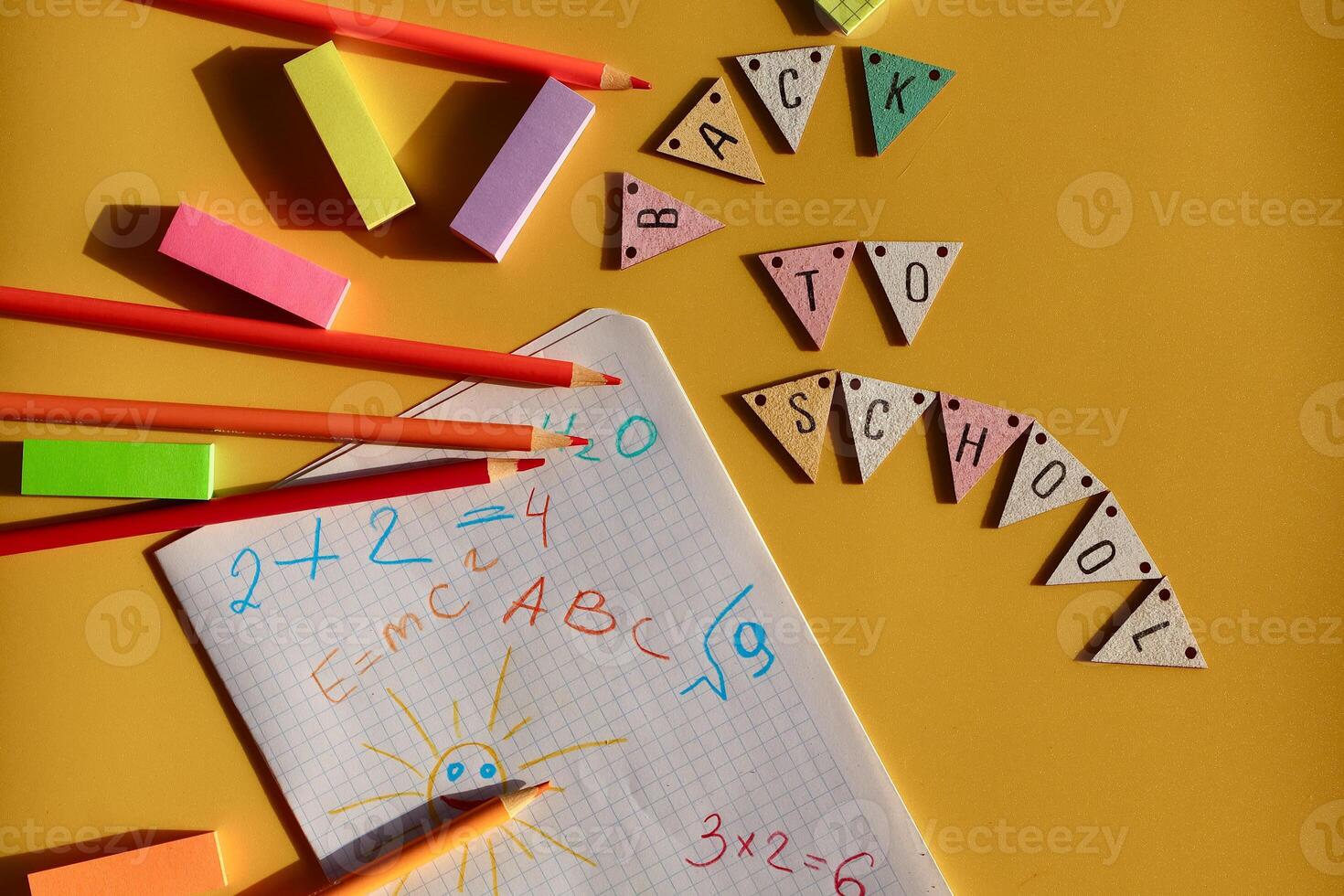 Back-to-school composition with pencils, sticky notes, and a math notebook on yellow background. Wooden bunting spells BACK TO SCHOOL colorful and fun. photo