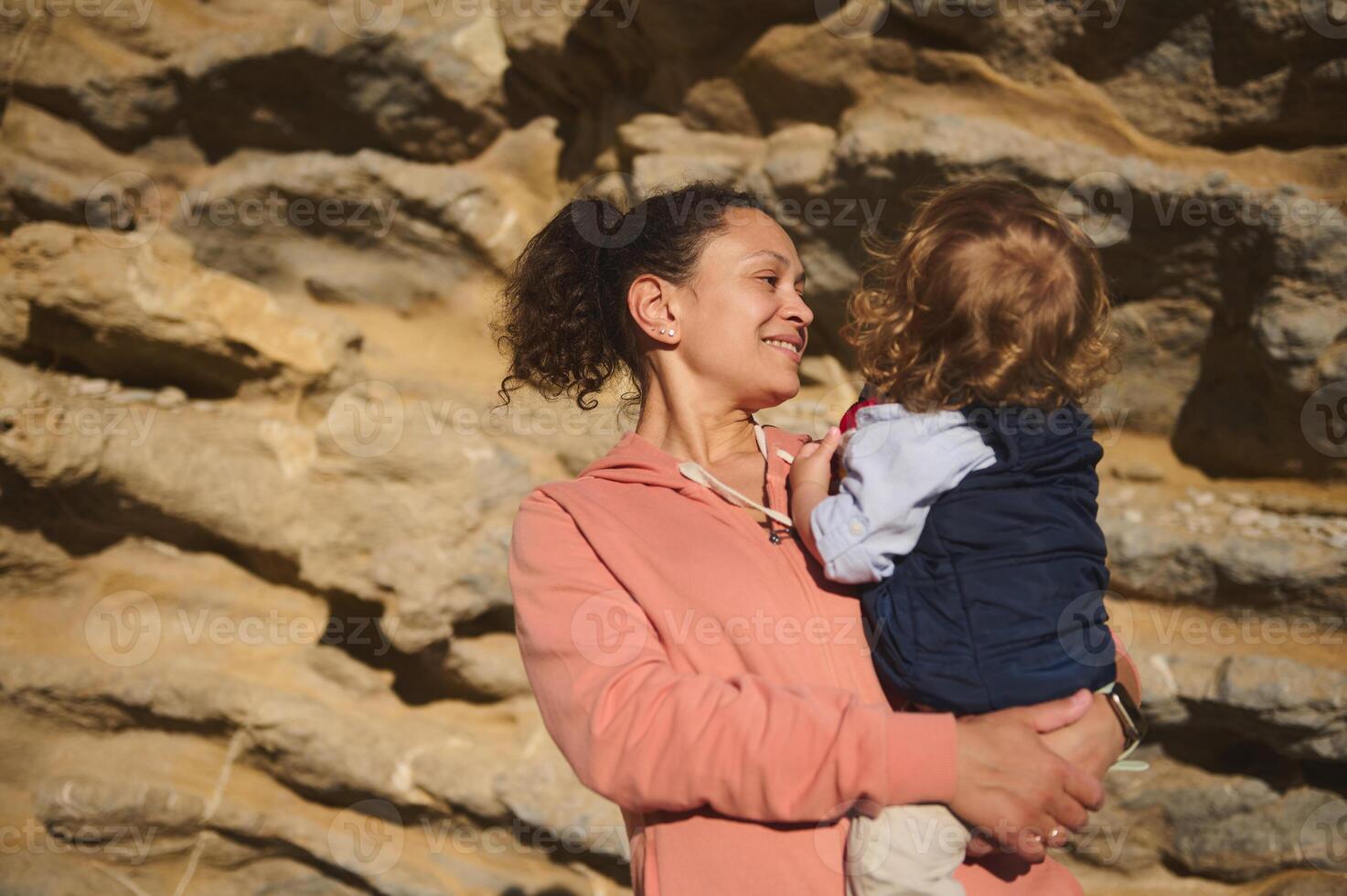 Smiling Woman Holding Child Outdoors Against Rock Wall Background photo