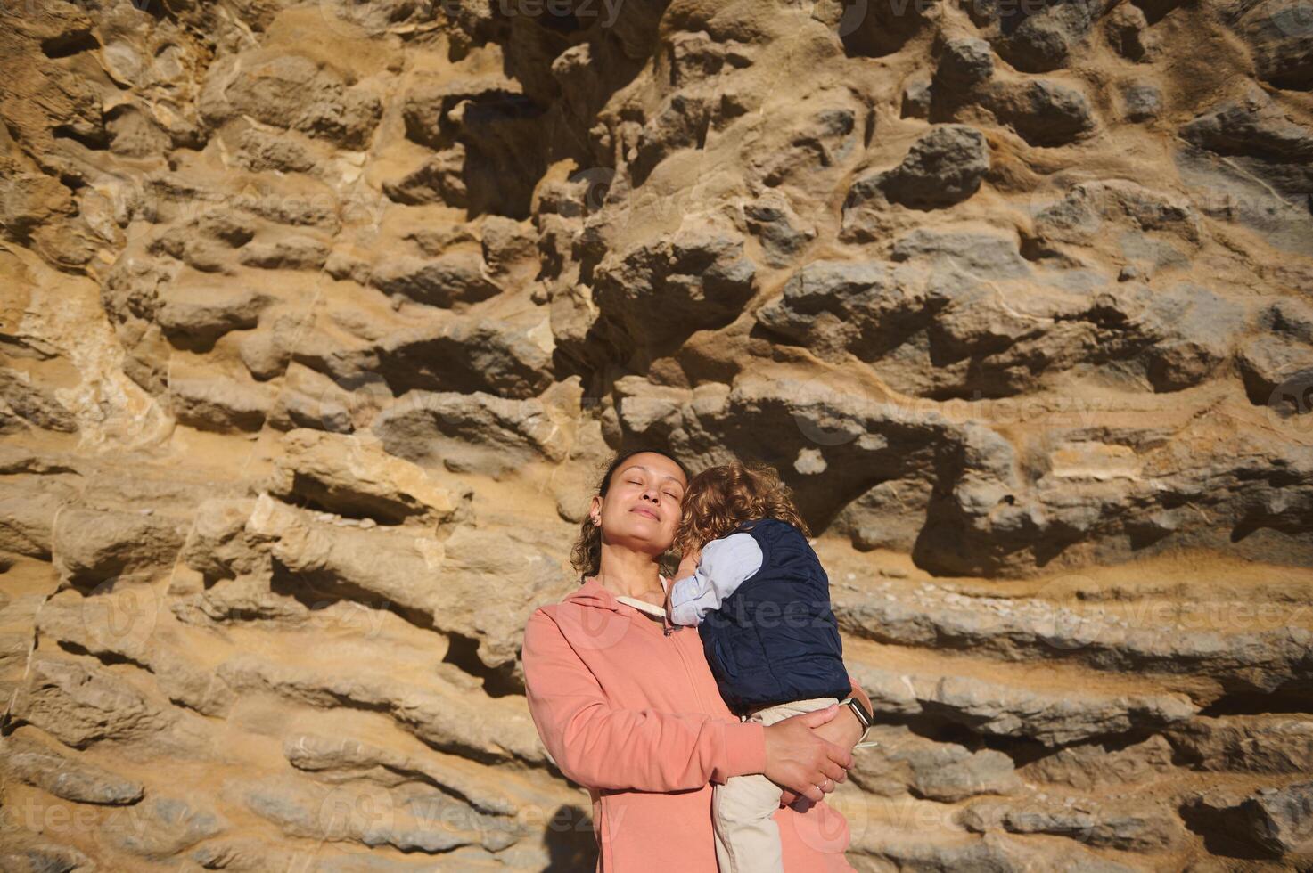 Mother Embracing Child Under Cliffside in Warm Light photo
