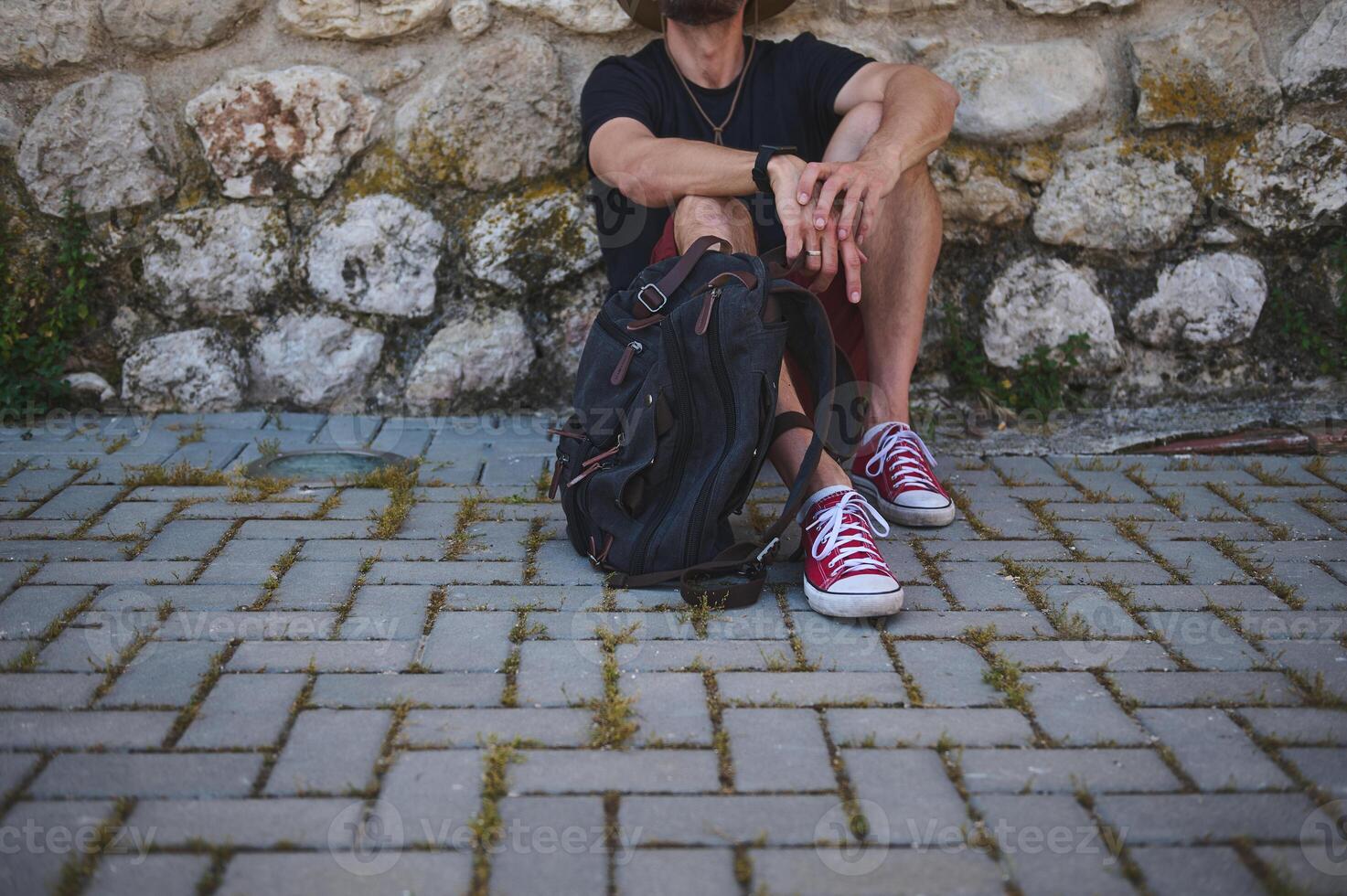 Traveler Seated Outdoors with Backpack Resting Against Rustic Stone Wall photo