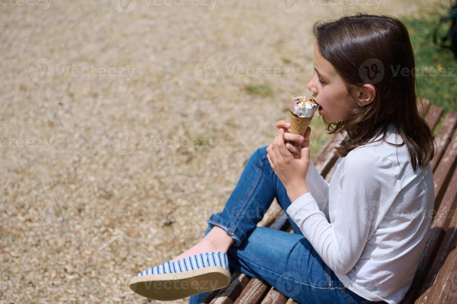 Young Girl Enjoying Ice Cream on a Park Bench in Sunny Weather photo