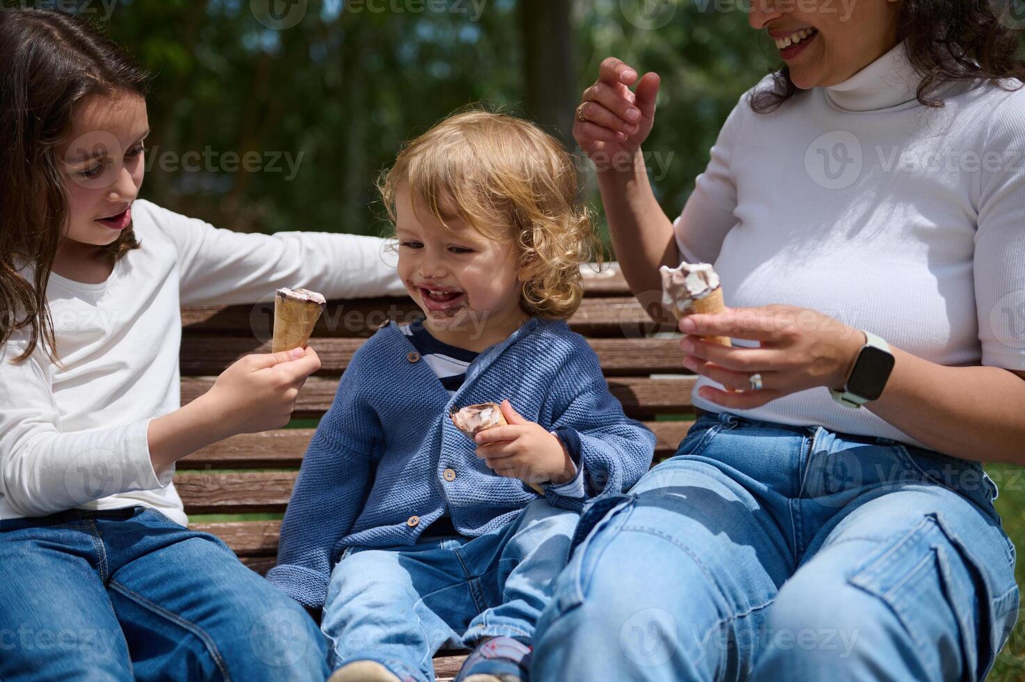 Family Enjoying Ice Cream Together on a Park Bench in the Sun photo