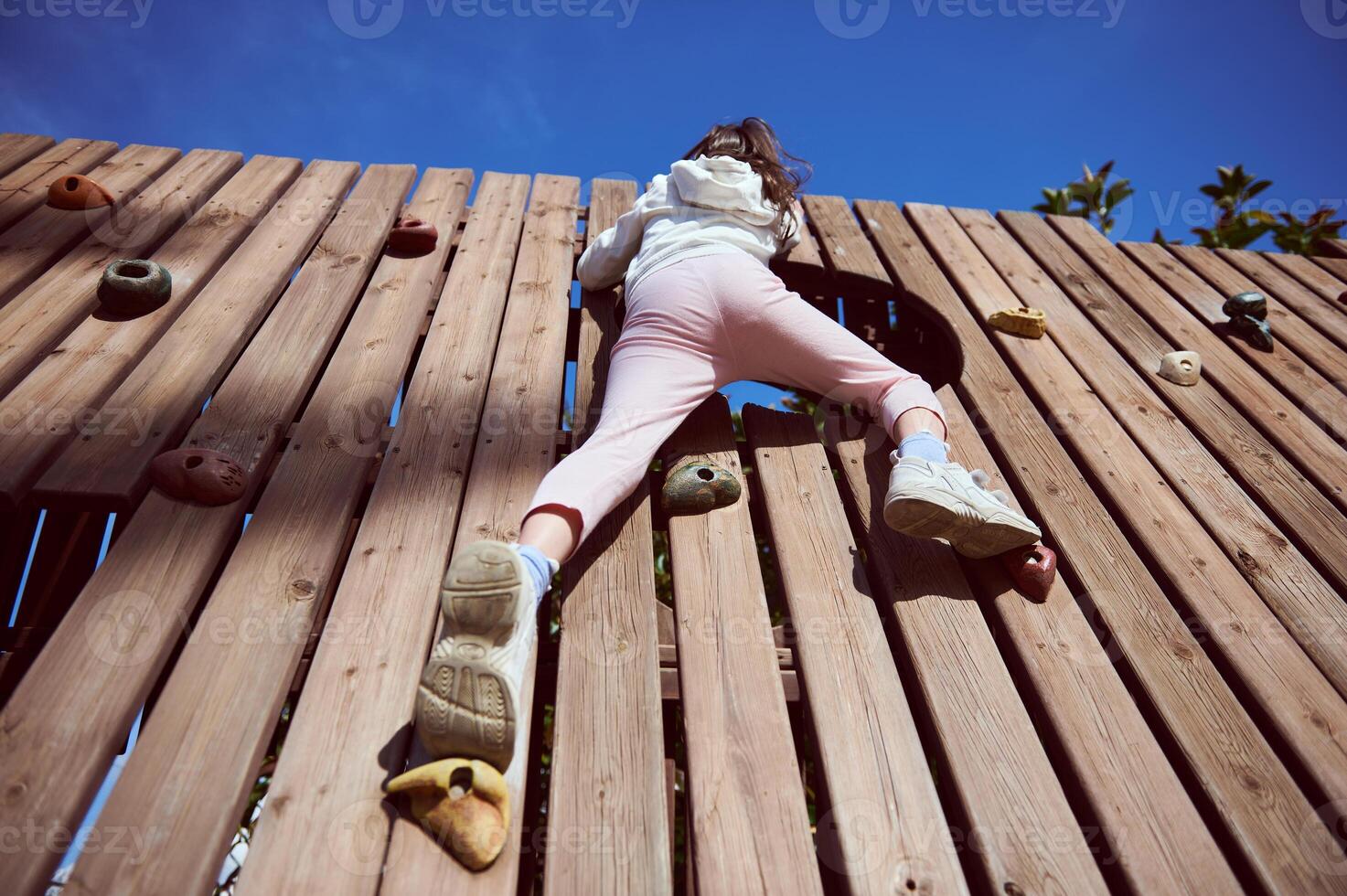 Rear View of a Child Climbing a Wooden Wall on a Sunny Day photo