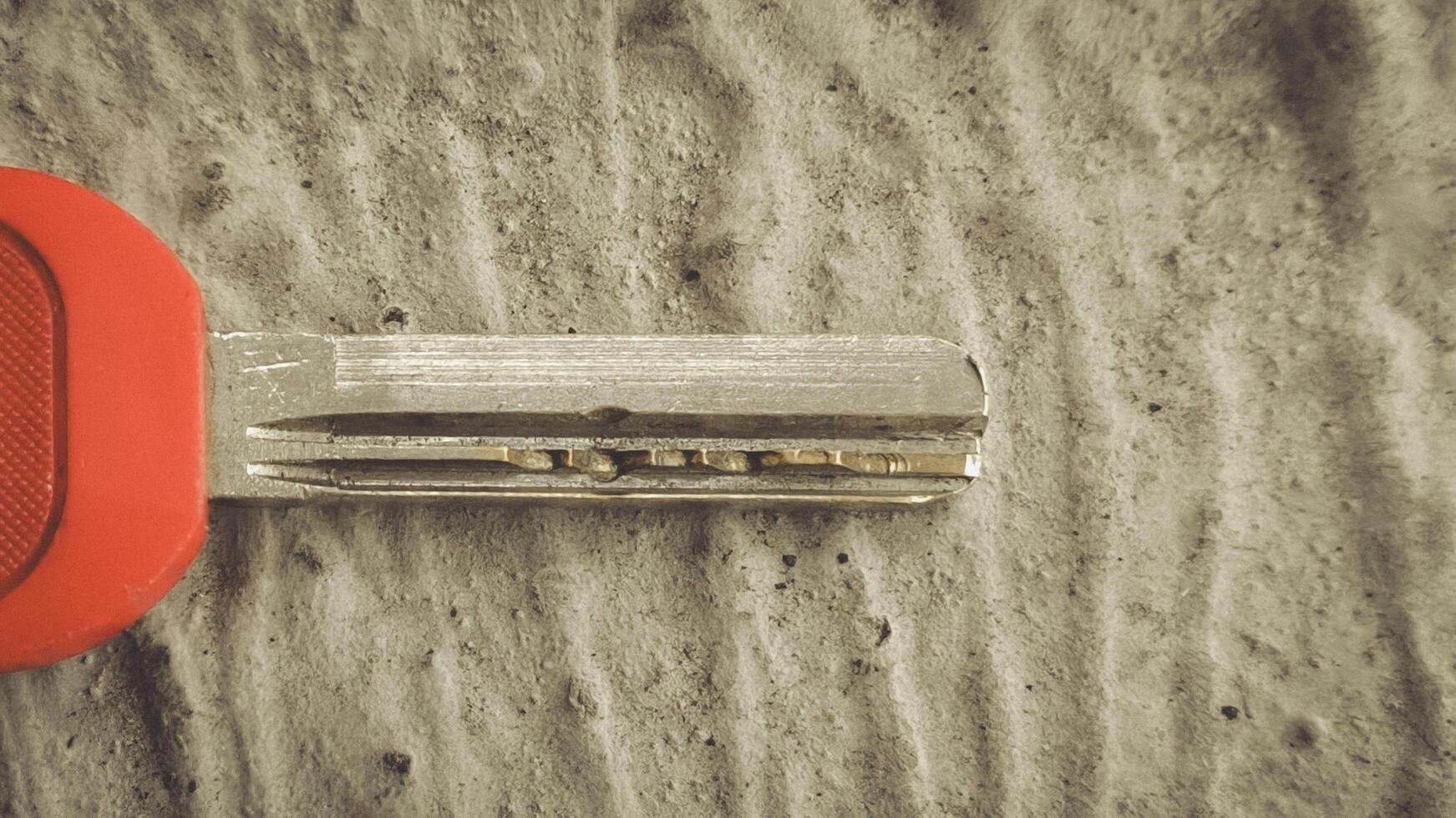Close-up of a Red-Handled Key Resting on Textured Concrete Surface photo