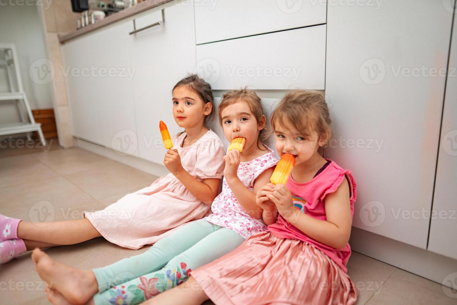 Three joyful girls enjoying colorful ice pops indoors photo
