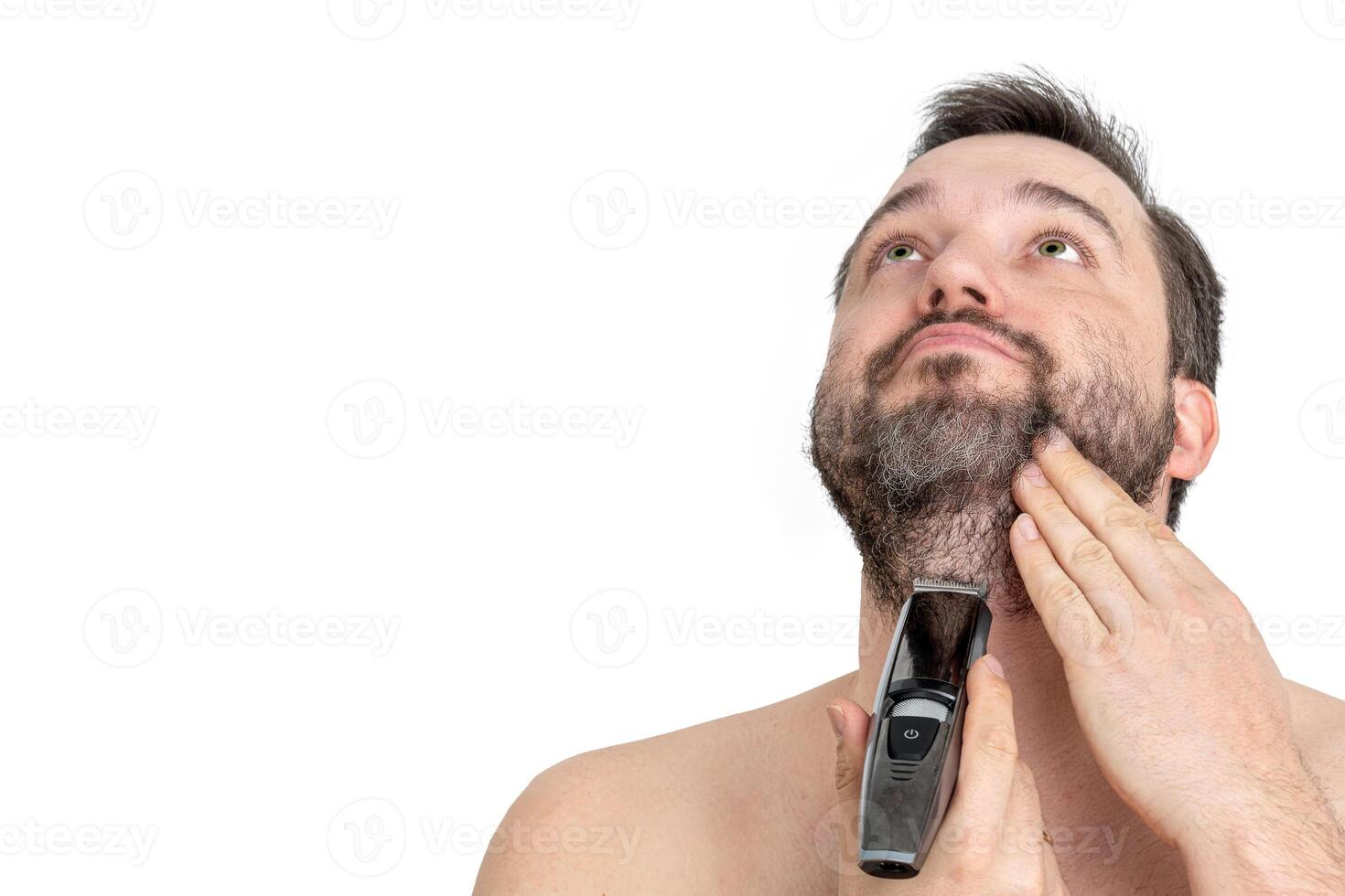 Close-up of a young man using an electric razor to shave his beard, against a white background. The man is carefully grooming his facial hair with a modern grooming tool. photo