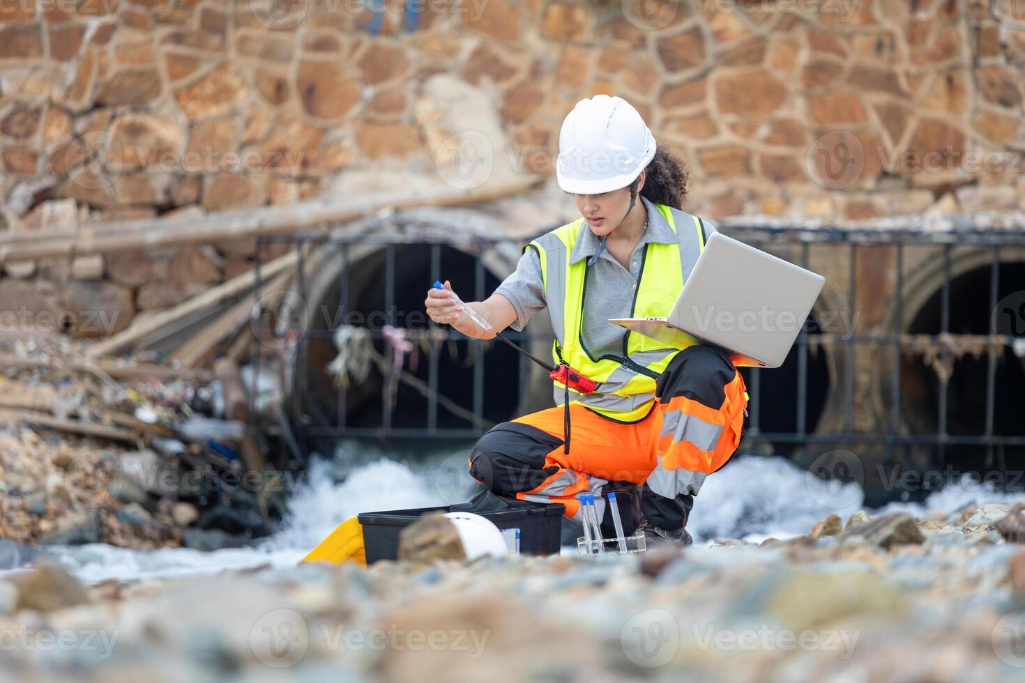 Environmental Engineer Testing Water Quality in Urban Drainage, Scientist Collecting Water Samples from Industrial Runoff, Female Technician Monitoring Water Pollution Near Concrete Pipes photo