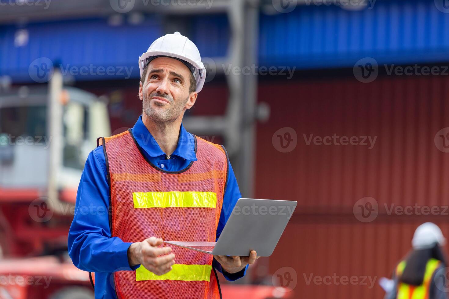 Engineer man with laptop inspecting containers box at shipping port, Foreman worker with blurred female engineer in background working at shipping yard photo