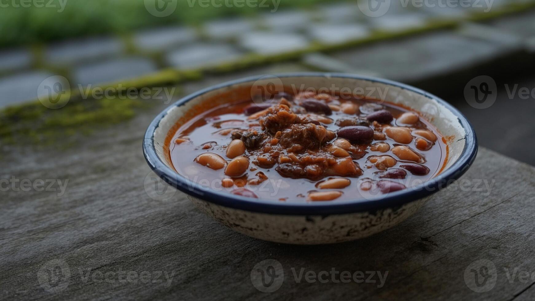 A bowl of chili and beans sitting on a wooden table photo