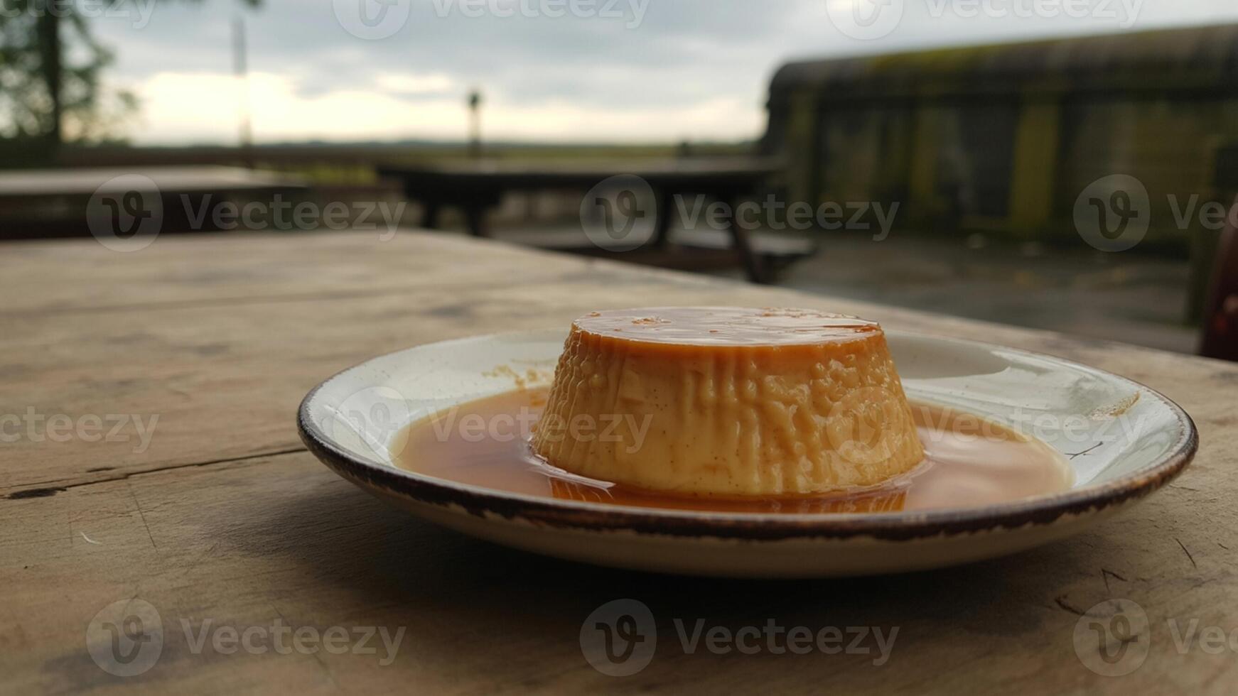 Caramel custard dessert on a plate sitting on a wooden table outside on a cloudy day in the distance photo