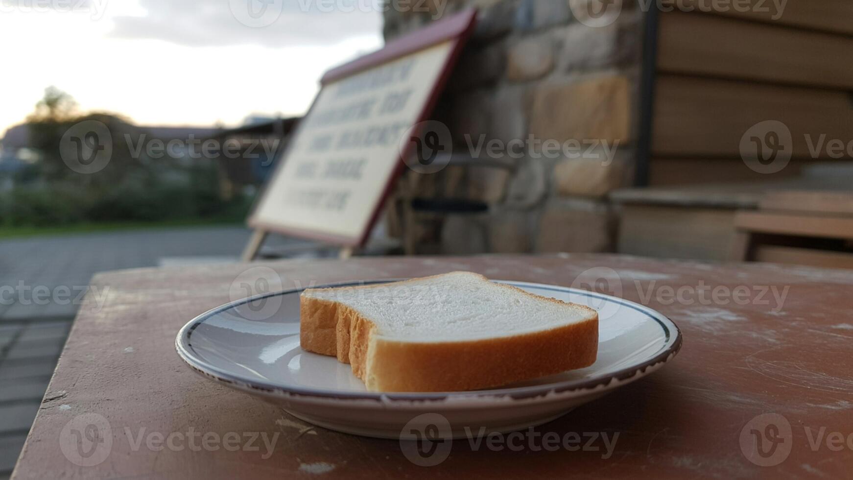 A slice of white bread on a plate sitting on a table outdoors with a building in the background photo