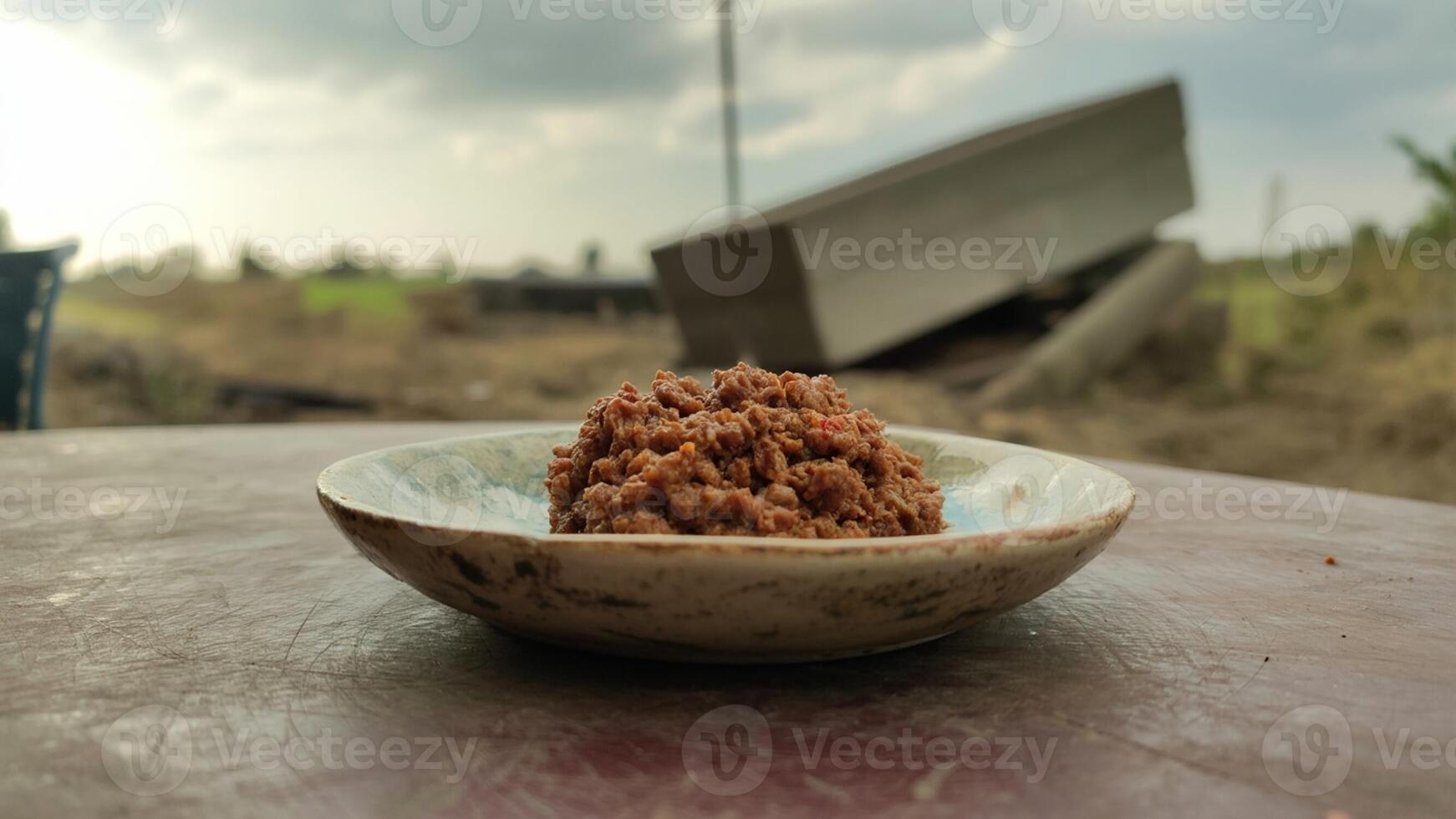 A plate of brown food sitting on a table with a blurry background of a cloudy sky and greenery photo