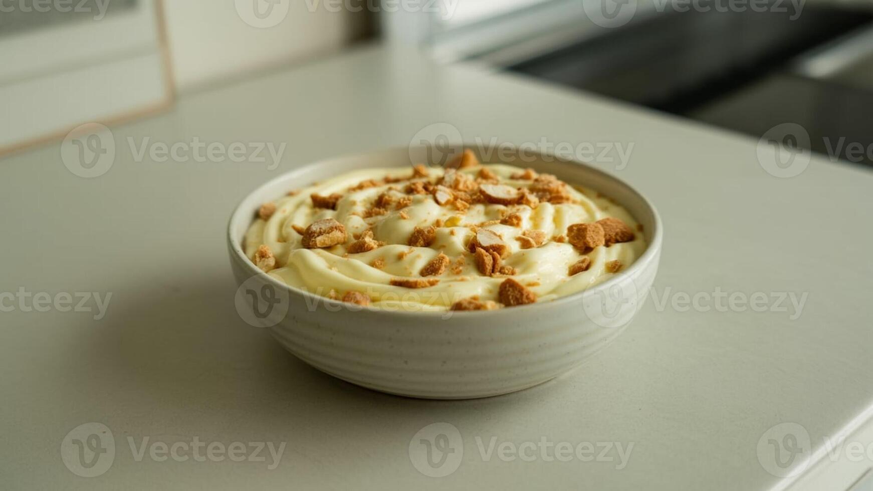 A close up shot of a bowl filled with a creamy dessert and topped with crunchy pieces on a gray surface photo