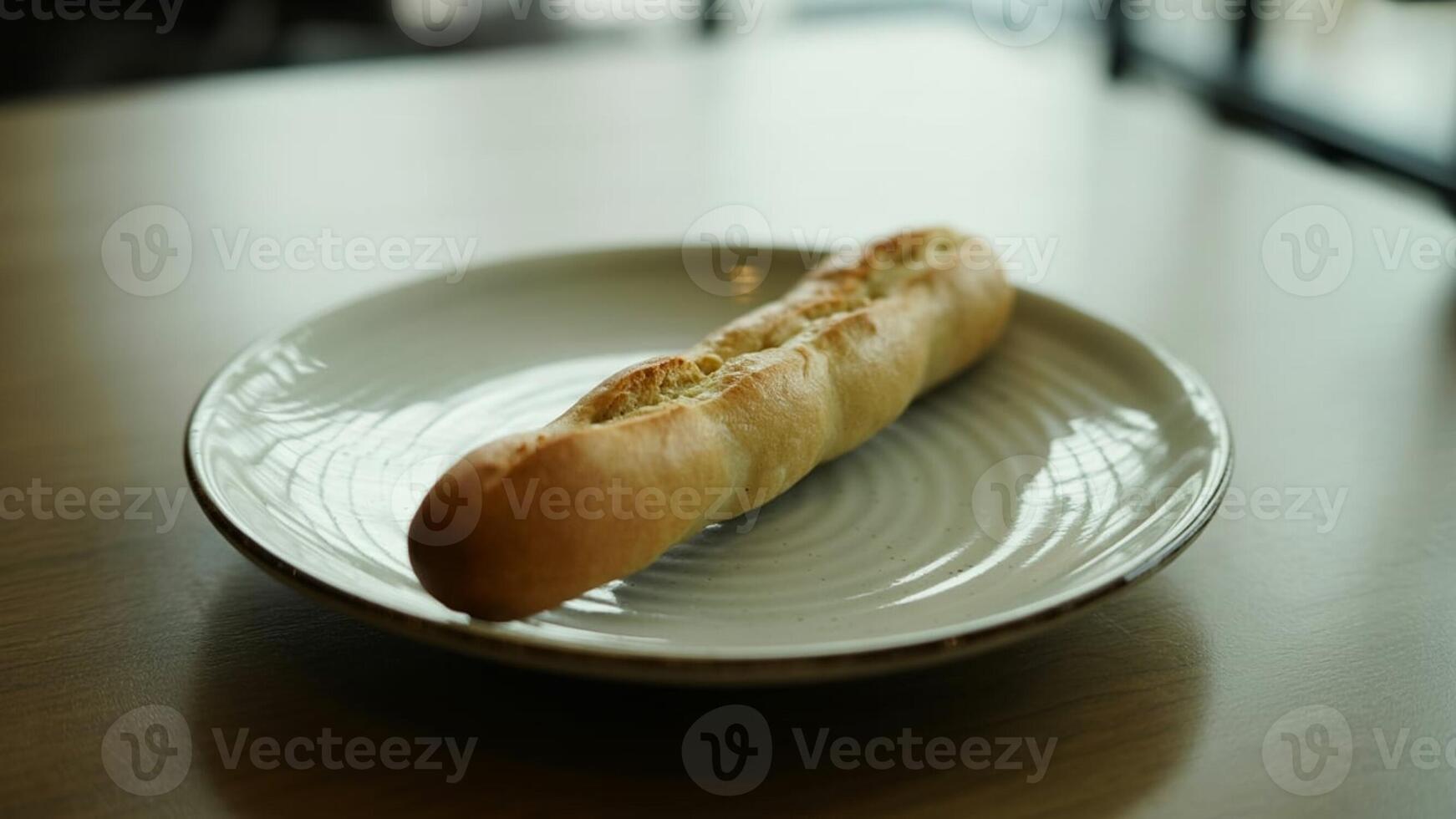 A baguette lying on a white plate on a table in a well lit area with a blurred background view photo
