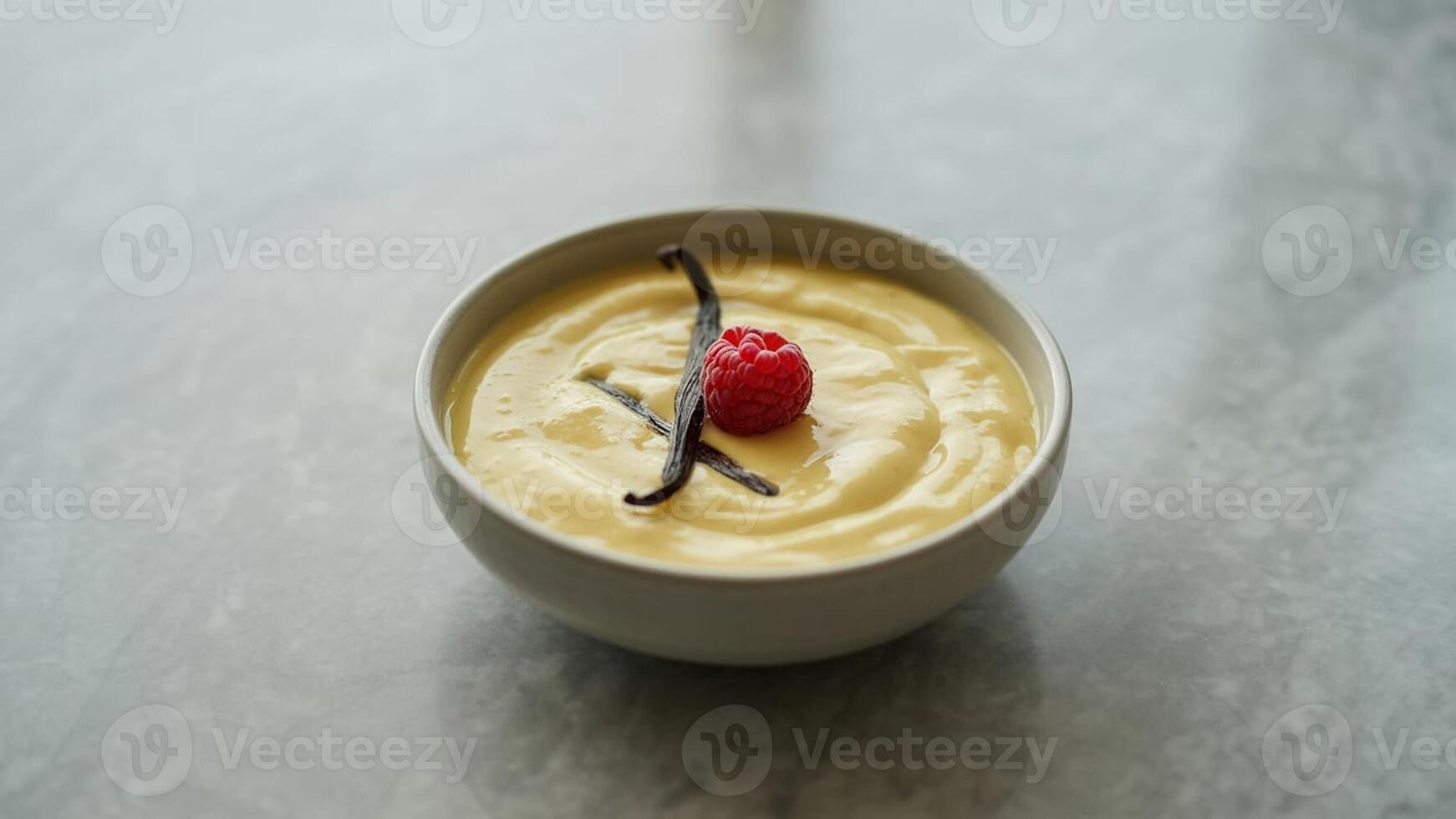 A bowl of yellow custard topped with a raspberry and vanilla beans on a light gray surface top view photo