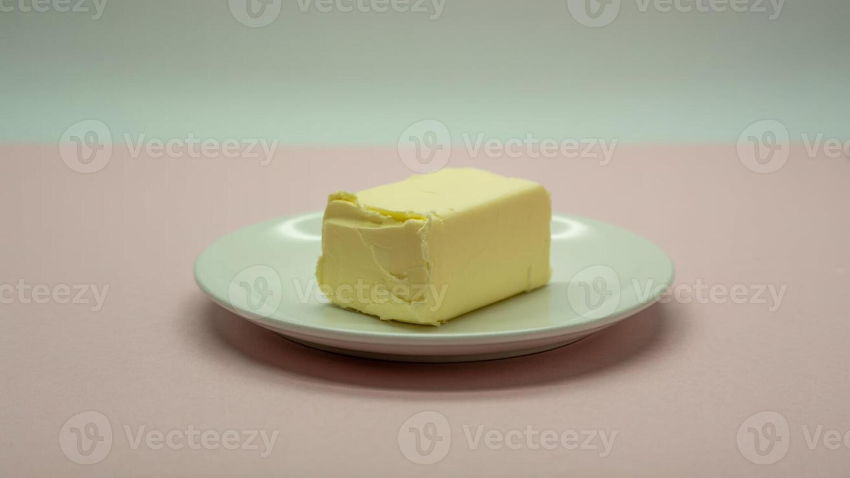 A block of butter sitting on a small white plate against a pink and white background in soft lighting photo