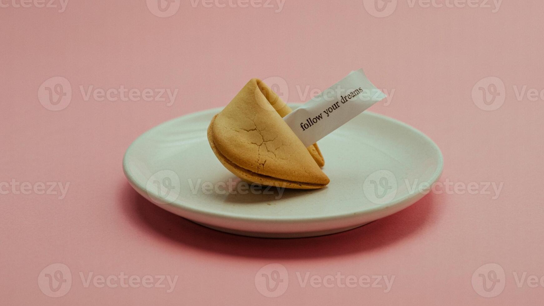 A fortune cookie on a white plate with a message that says follow your dreams on a pink background photo