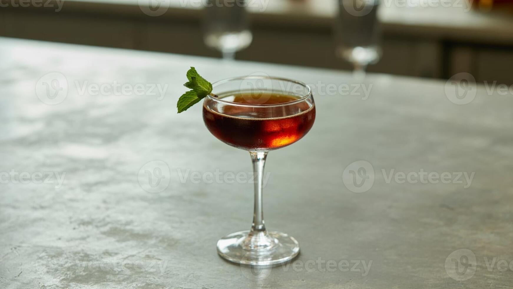 A single cocktail glass with a dark drink and mint garnish on a gray surface with blurred background photo