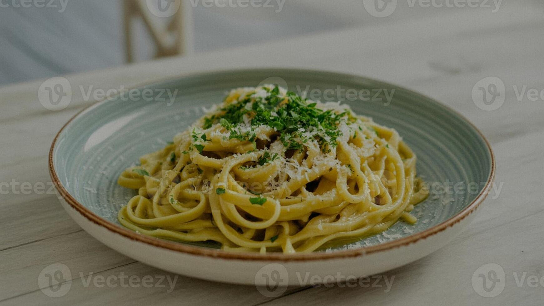 a pla te of crea my pa sta dish with pa rsley a nd pa rmesa n cheese on a wooden ta ble nea r a white linen photo