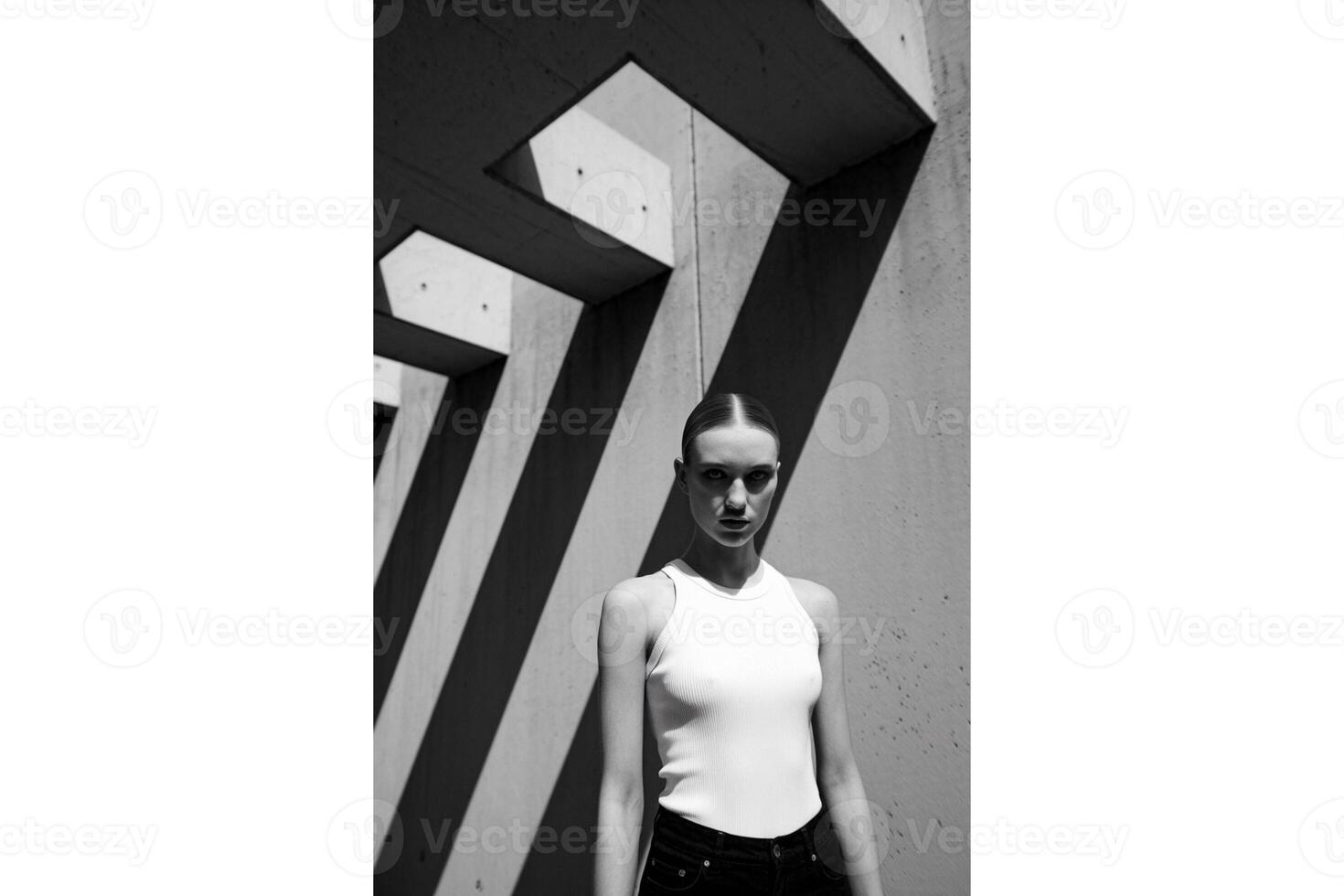 Woman in white tank top standing near concrete structure in black and white art photo