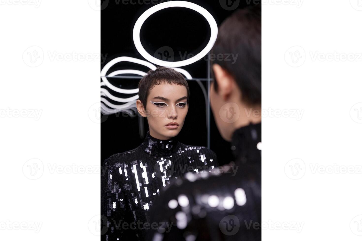 Woman with white eyeliner and sequined top reflected in a mirror with neon lights photo