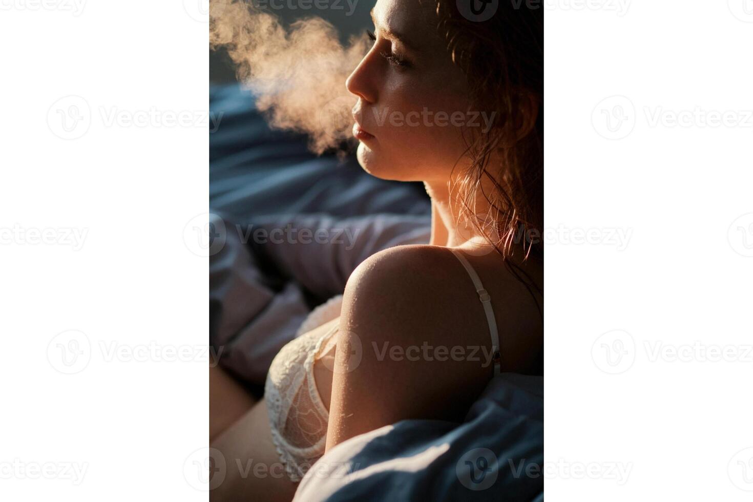 Profile view of a woman exhaling smoke in bed with sunlight on her face and hair photo