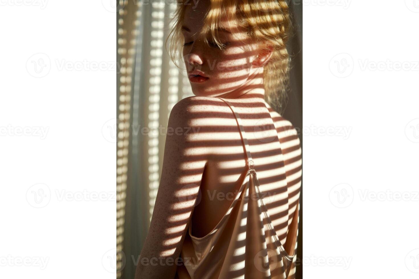 A woman in a slip dress stands in sunlight with shadows across her face and body photo