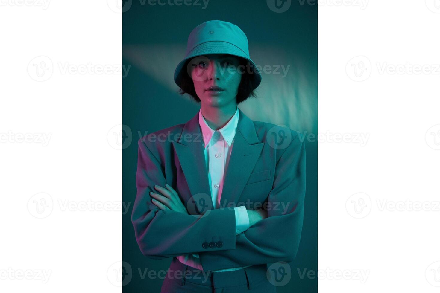 A woman with crossed arms wearing a bucket hat and suit under colorful lighting photo