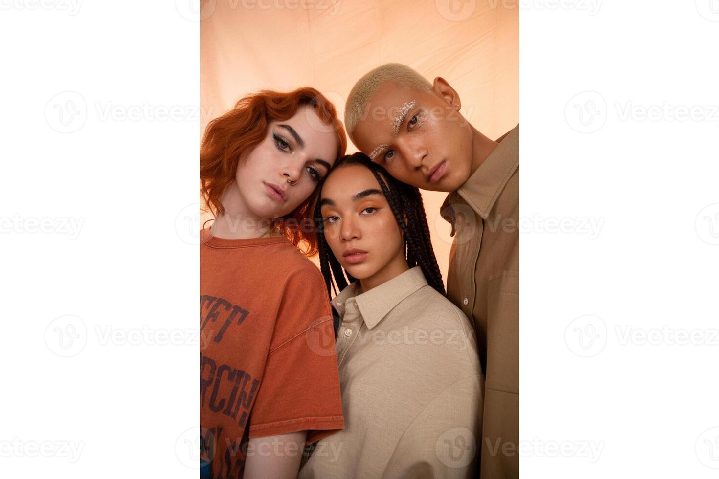 Three diverse models posing closely together in front of a peach colored backdrop photo