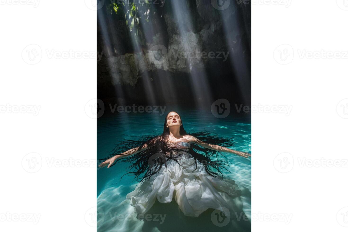 Woman in white dress floating in turquoise water with sunlight streaming down above photo