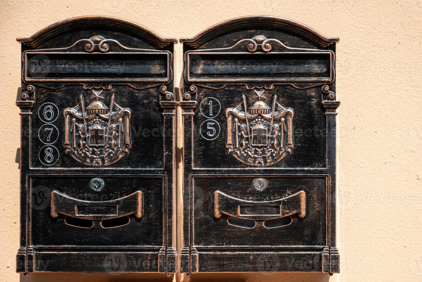 Vintage-style metal mailboxes mounted on a wall. Each box features ornate decorations with a crest. photo