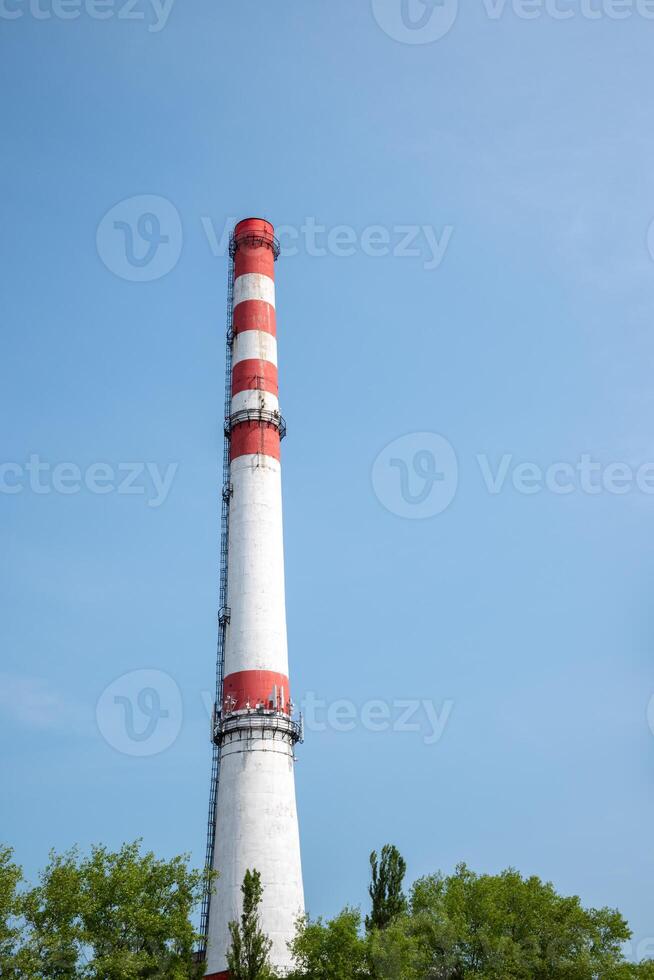 Tall industrial chimney with red and white stripes, extending into a clear blue sky. photo