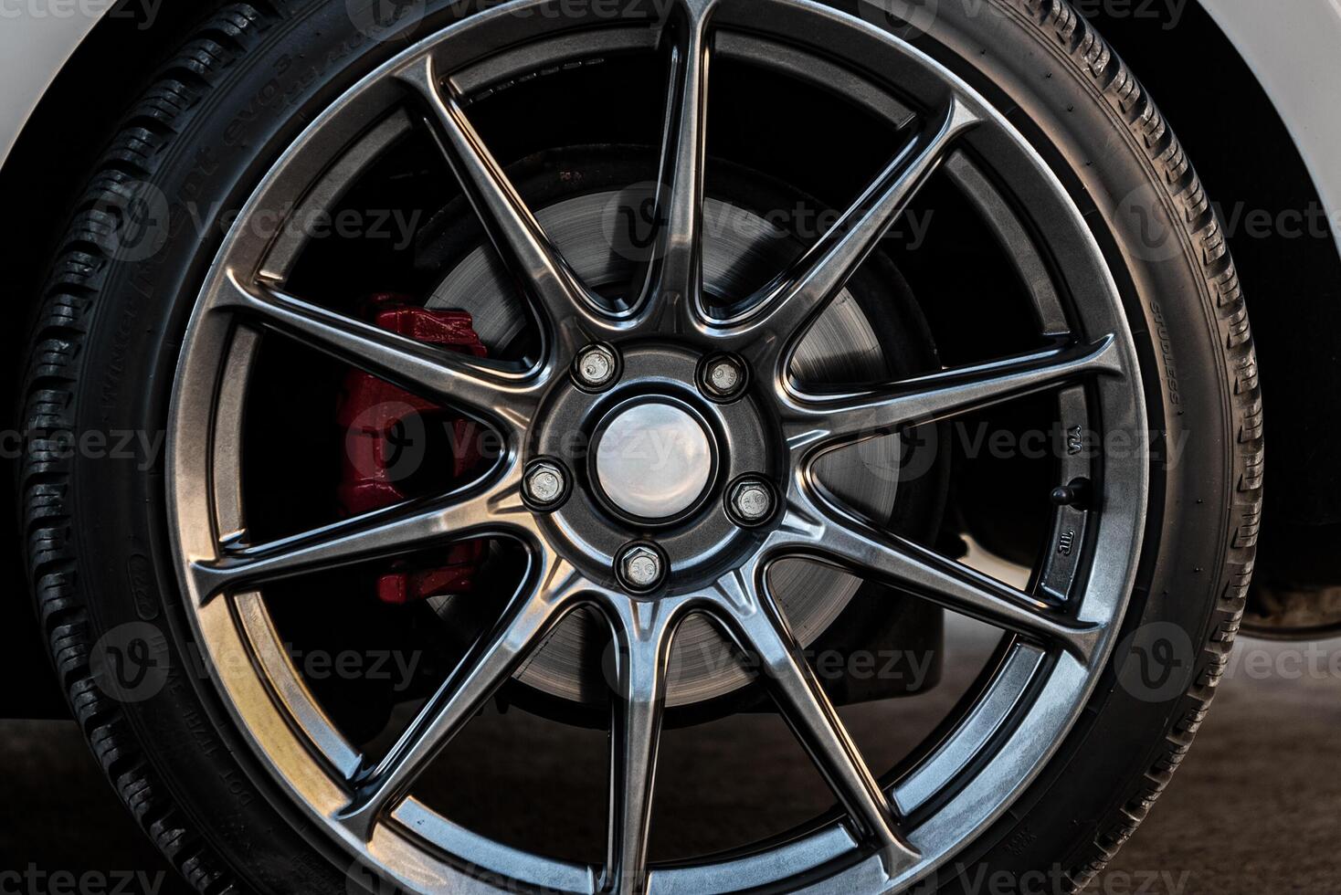 A close-up of an alloy car wheel featuring a multi-spoke design. The metallic spokes have a dark, polished finish, contrasting with the silver center cap. photo