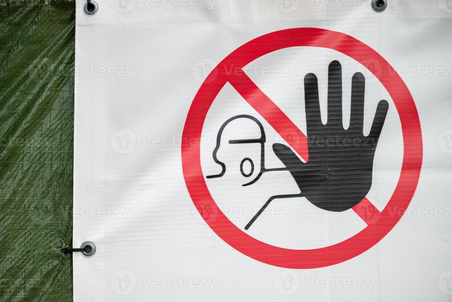 A safety sign with a red circular border and diagonal slash features a black hand symbol and a helmeted figure. photo